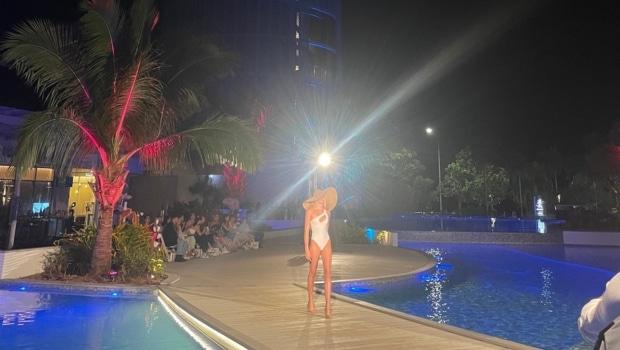 A model walks the runway at Cairns Fashion Week in swimwear and a large hat.